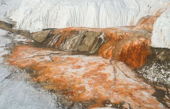 Blood Falls - Victoria Land, East Antarctica The outflow of this reddish plume of water from the edge of Taylor Glacier in McMurdo Dry Valleys in Victoria Land, East Antarctica is a sight like no other. Scientists initially thought the red color was due to some form of algae but later found it was because of the presence of salinity and iron that give the water its color. Almost two million years ago, the glacier sealed a small water body containing an ancient community of microbes, below a layer of ice that metabolizes sulfate and ferric ions in it to survive.